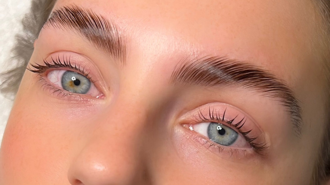 Nahaufnahme von Augen mit blauen Pupillen, dichten Brauen und dezentes Makeup.