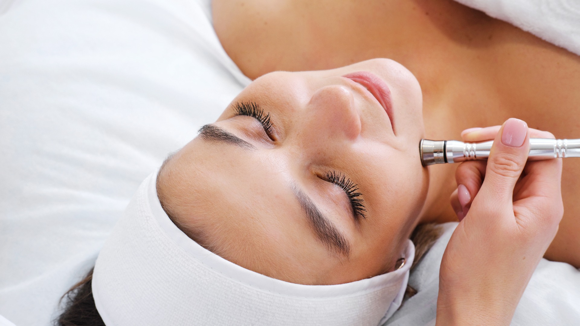Die Kosmetikerin führt die Mikrodermabrasion der Gesichtshaut einer schönen, jungen Frau in einem Schönheitssalon durch. Kosmetologie und professionelle Hautpflege.