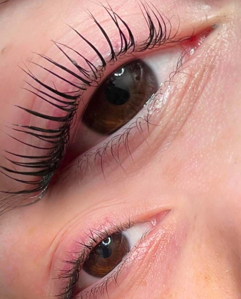 Nahaufnahme von zwei braunen Augen mit langen Wimpern und rosafarbener Haut.