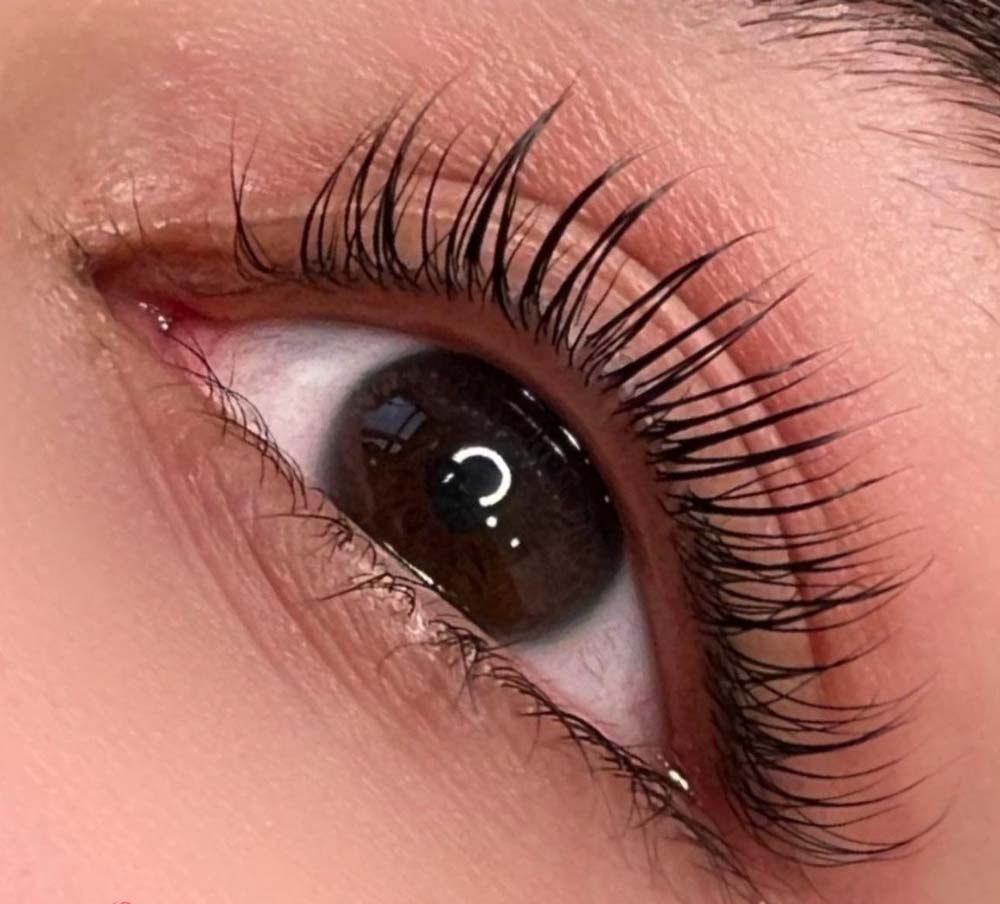 Nahaufnahme eines Auges mit langen, geschwungenen Wimpern und brauner Iris.